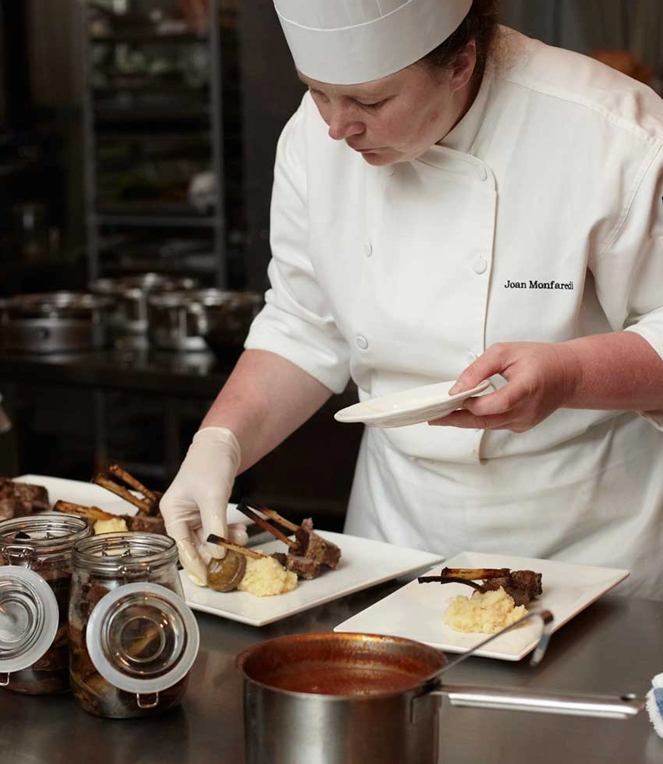 Joan Monfaredi of Two13 Food Design plating a high end, fine dining dish in a kitchen setting.