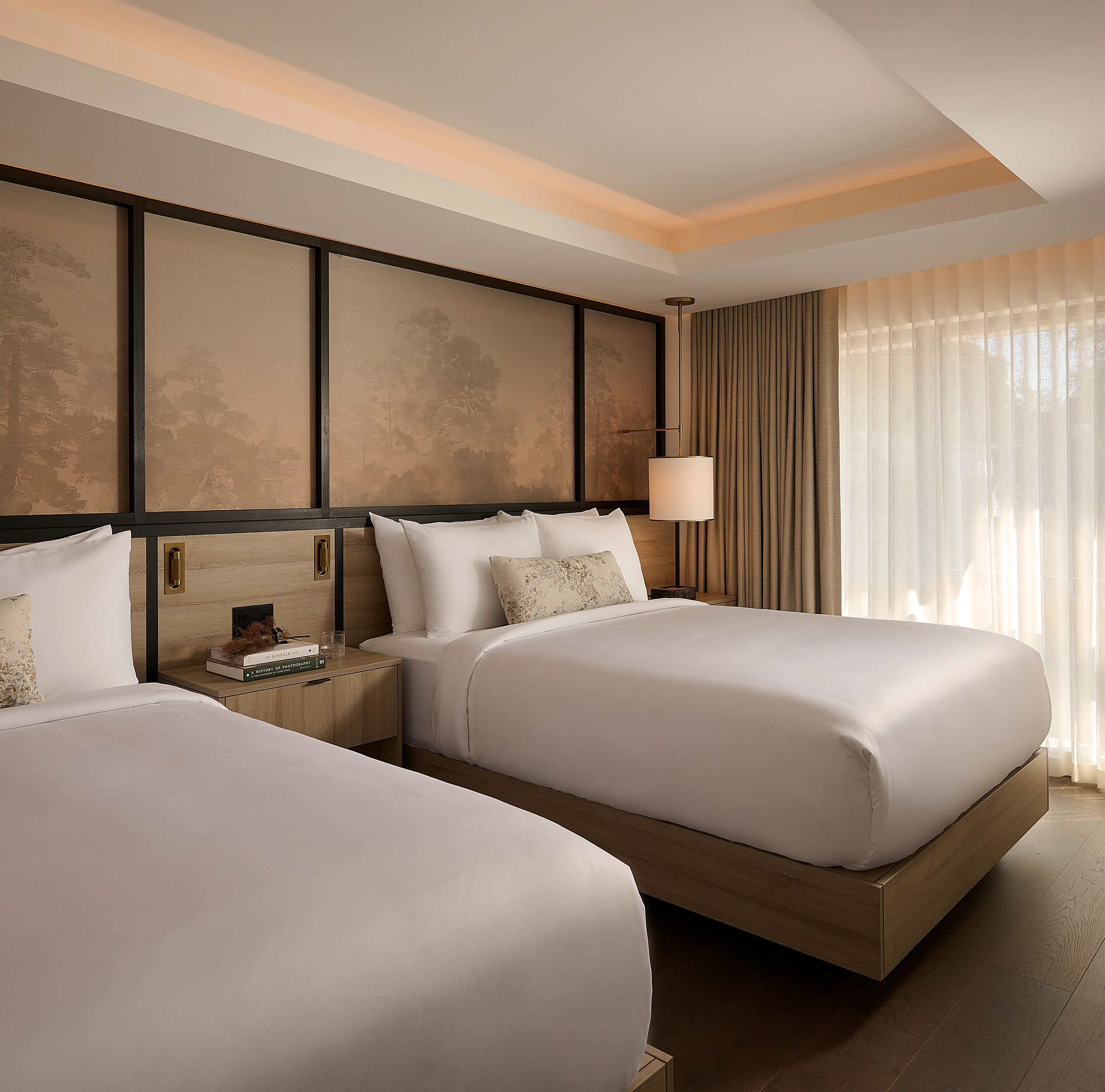 A view of a luxury hotel suite at Glenhill Hotel North York featuring two queen-size beds with premium white linens, boutique finishes and high-end lighting throughout the living space.