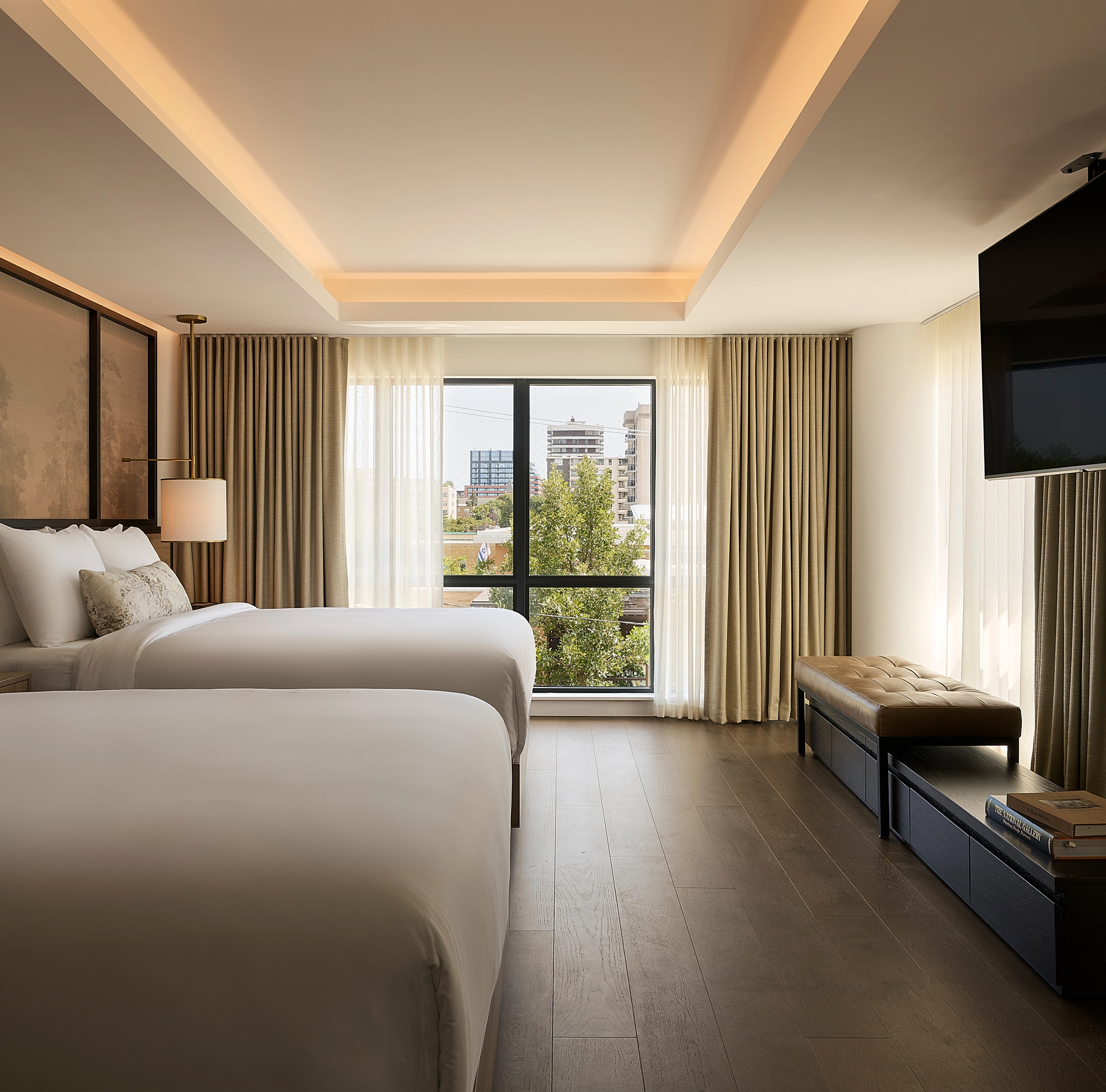 A view of a luxury hotel suite at Glenhill Hotel North York featuring two queen-size beds with premium white linens, boutique finishes and high-end lighting throughout the living space.